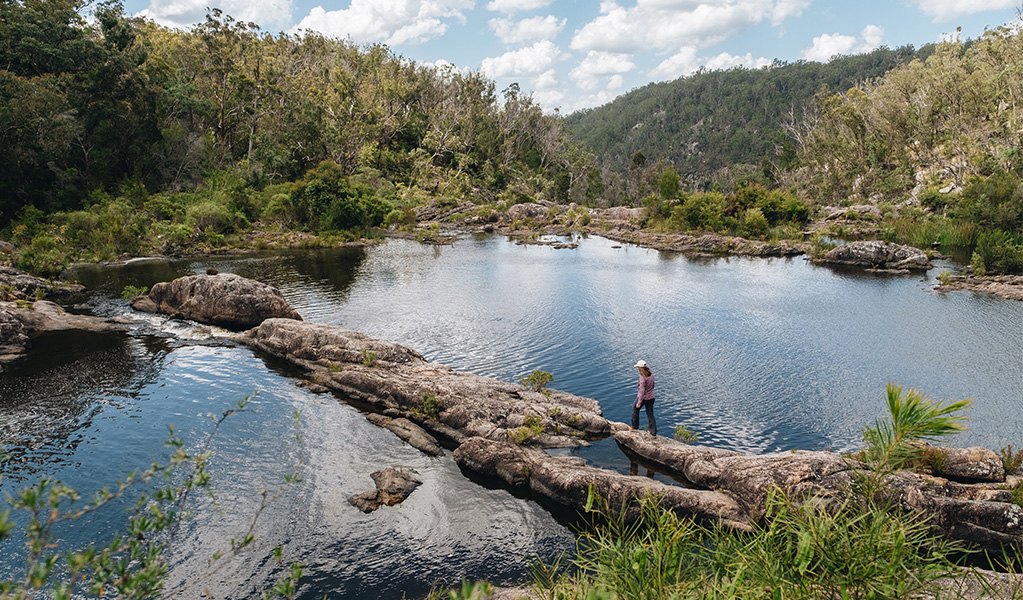 Person walking over rocks by rockpools in Boonoo Boonoo National Park. Photo: Harrison Candlin &copy; DCCEEW