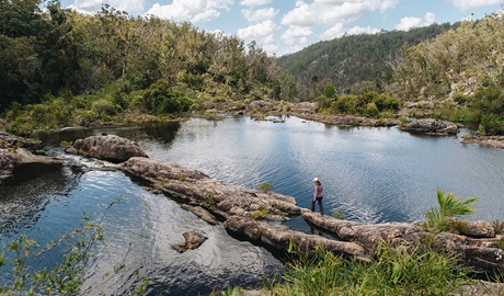 Person walking over rocks by rockpools in Boonoo Boonoo National Park. Photo: Harrison Candlin &copy; DCCEEW