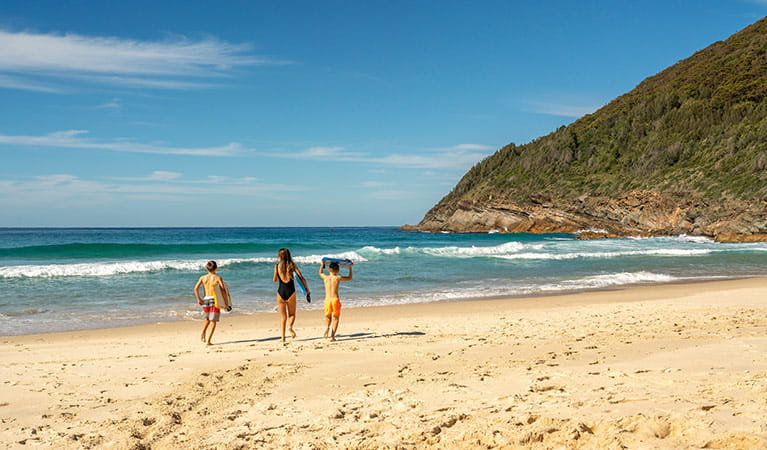 A woman and two children run towards the sea on a beach, Booti Booti National Park. Photo credit: John Spencer &copy; DPIE