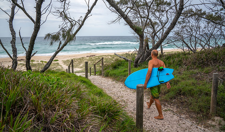 A surfer walks along a sandy beach track near Santa Barbara picnic area in Booti Booti National Park. Photo credit: John Spencer &copy; DPIE