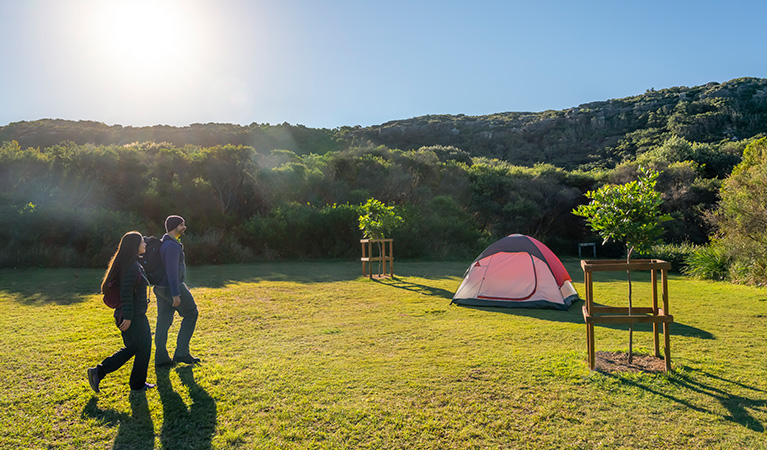 2 hikers walking to their tent at Tallow Beach camground, Bouddi National Park. Photo: John Spencer/DPIE.