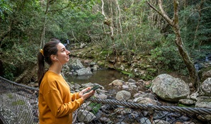 A woman listens to an audio tour on her mobile phone with headphone at Minnamurra Rainfores. Photo: John Spencer &copy; DPIE