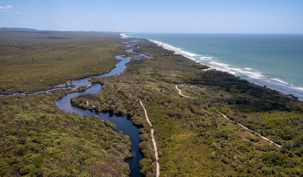 Aerial view of Jerusalem Creek, the lush green country surrounding it with walking tracks running through it and the ocean breaking into surf on the coast to the east, Bundjalung National Park. Credit: John Spencer/DCCEEW &copy; DCCEEW