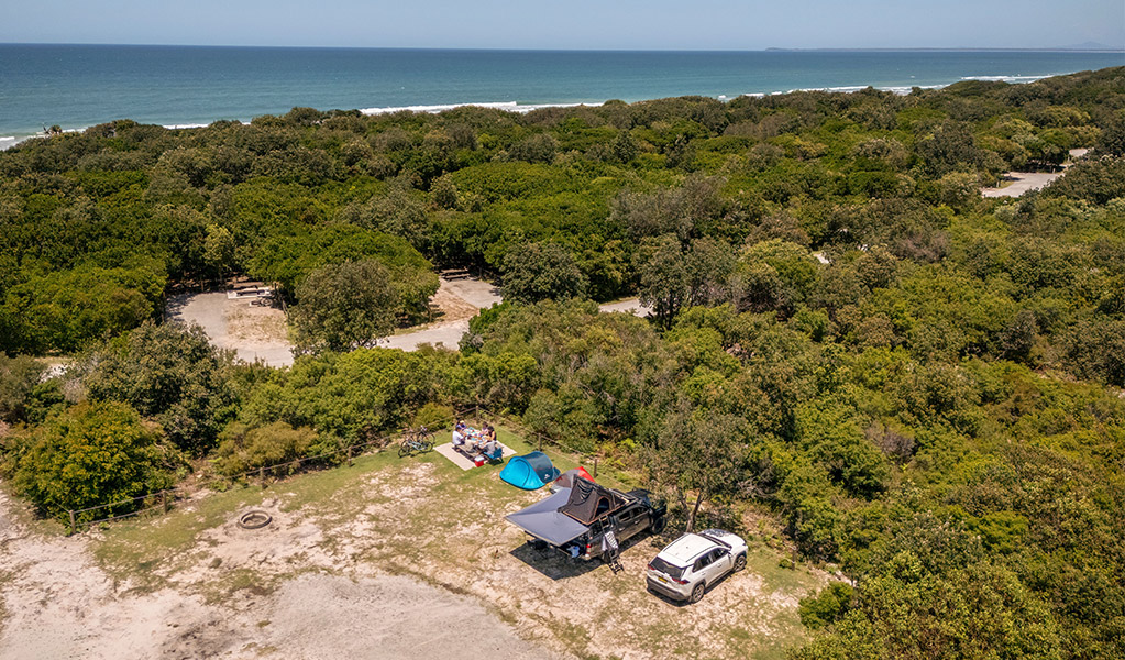 A group of campers camping beside their vehicle at Mibanbah-Black Rocks campground, the ocean in the distance. Credit: John Spencer &copy; DCCEEW