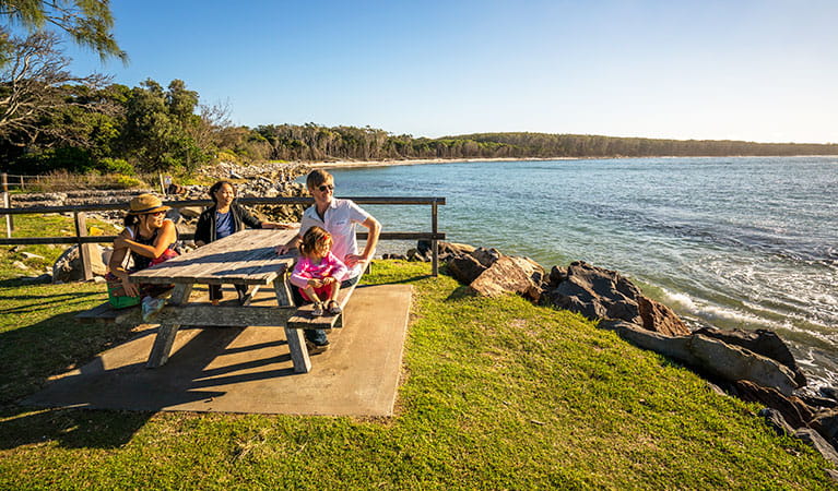 A group at a picnic table by the water, Woody Head campground, Bundjalung National Park. Photo: John Spencer/OEH
