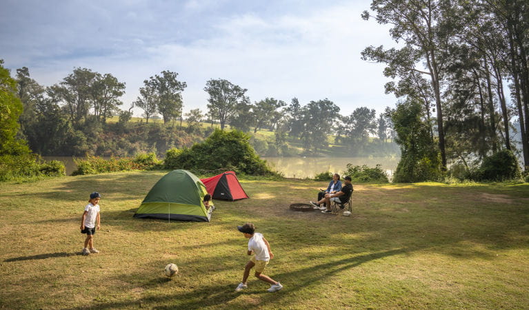 Parents sit outside their tent beside the Hawkesbury River while their kids play soccer, at Cattai campground in Cattai National Park. Photo: John Spencer/OEH
