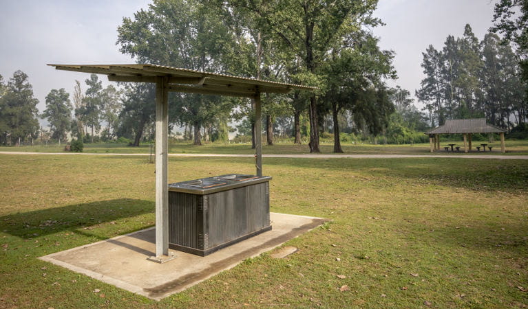 An electric barbecue underneath a shelter, with a picnic shed in the background, at Cattai Farm picnic area in Cattai National Park. Photo: John Spencer/OEH