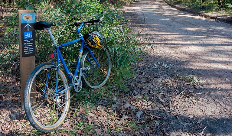A bike rests against a sign beside a trail in Conjola National Park. Photo: Michael Van Ewijk &copy; DPIE