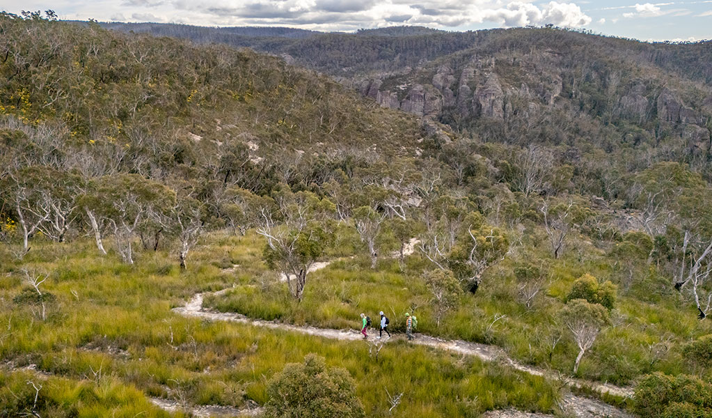 3 people walking on Broad Swamp to Birds Rock walking track with pagoda formations in the background. Credit: John Spencer &copy; DCCEEW