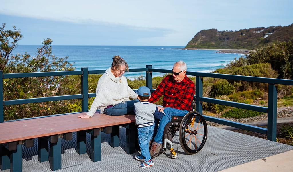 A man in a wheelchair with a woman and a young child at Dudley Beach, Glenrock State Conservation Area. Photo: Jared Lyons &copy; DPE