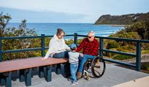 A man in a wheelchair with a woman and a young child at Dudley Beach, Glenrock State Conservation Area. Photo: Jared Lyons &copy; DPE