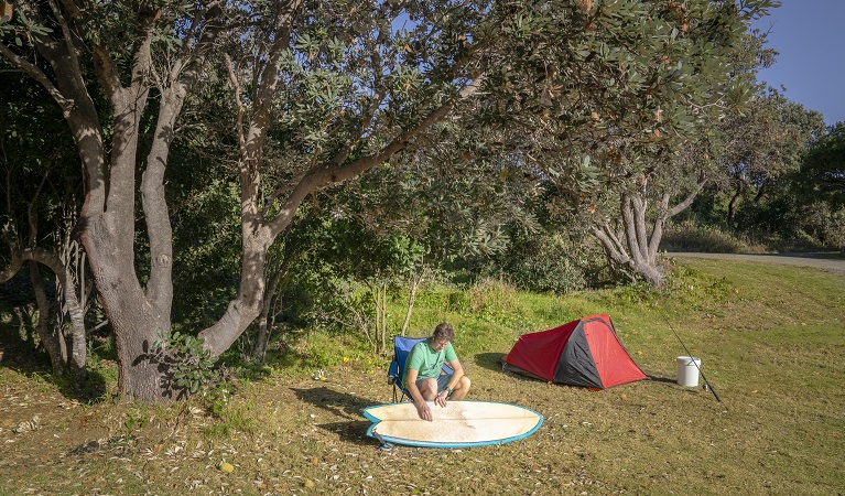 A man cleaning his surf board at Racecourse campground, Goolawah National Park. Photo: John Spencer/OEH