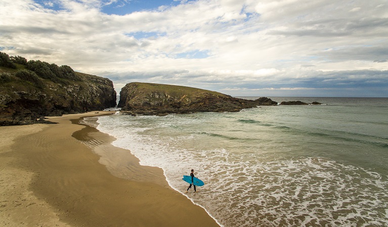 A surfer with his board walking along the beach into the ocean at Goolawah National Park. Photo: John Spencer/OEH