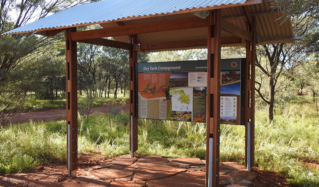 Photo of sign about Dry Tank campground under a shelter surrounded by trees, grass and red dirt at Gundabooka National Park. Photo credit: Jess Ellis/DPE &copy; DPE