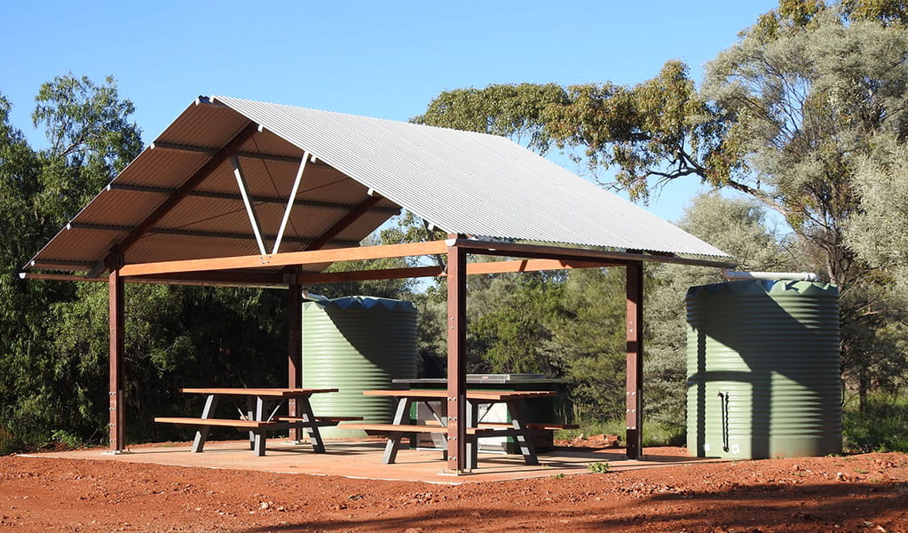 Photo of picnic tables and a barbecue under a shelter surrounded by trees and red dirt at Gundabooka National Park. Photo credit: Jess Ellis/DPE &copy; DPE