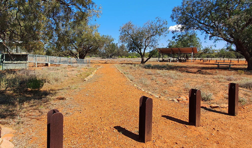 Wide view of a picnic table with a shelter next to toilet facilities in an outback setting of red earth and scattered trees. Photo credit: Jessica Ellis &copy; DPIE