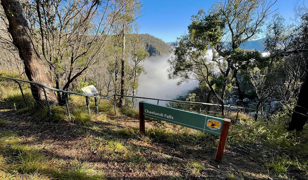 View past park signage and metal safety railing to a cloud filled mountain valley. Photo &copy; Tina Sullivan