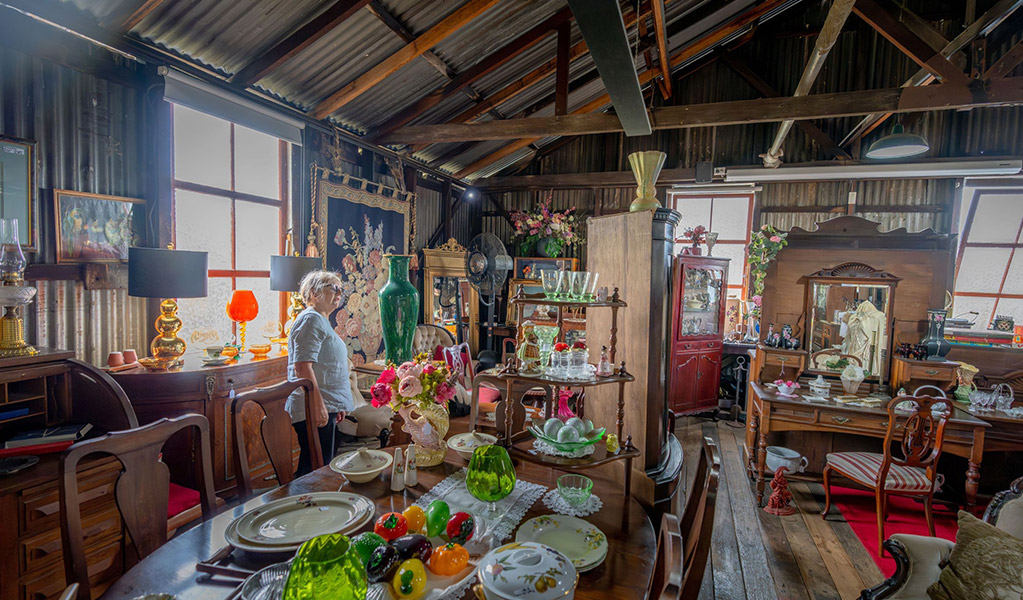 A visitor looking at an antique green vase surrounded by antiques for sale at Gold Rush Antiques in the historic Corneys Garage. Credit: John Spencer &copy; DCCEEW