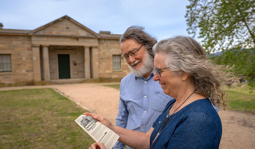 2 people reading a pamphlet in front of Hartley Courthouse at Hartley Historic Site. Credit: John Spencer &copy; DCCEEW