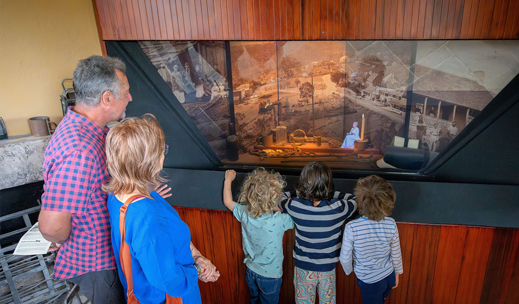 2 adults and 3 kids watching a hologram re-enactment of the historic court process inside Hartley Courthouse. Credit: John Spencer &copy; DCCEEW