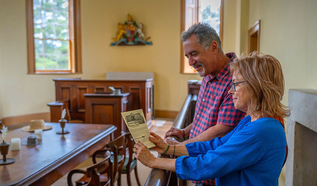 2 people reading a pamphlet inside Hartley Courthouse at Hartley Historic Site. Credit: John Spencer &copy; DCCEEW