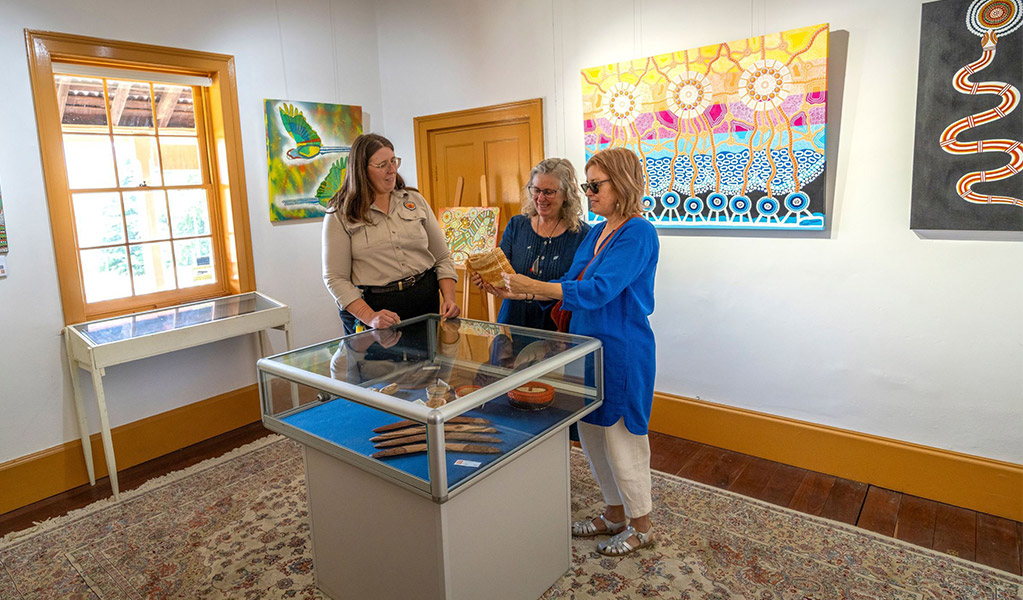 2 visitors and an NPWS staff member surrounded by Aboriginal artworks inside Kew-Y-Ahn Aboriginal Art Gallery, Hartley Historic Site Visitor Centre. Credit: John Spencer &copy; DCCEEW