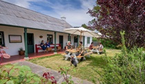 People eating at shaded tables on the lawn and garden outside The Postmistress Cafe and Store at Hartley Historic Site. Credit: John Spencer &copy; DCCEEW