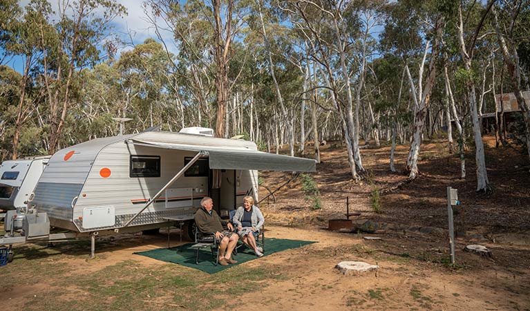 A couple sit outside their caravan in camping chairs, at Glendora campground in Hill End Historic Site. Photo: John Spencer/OEH