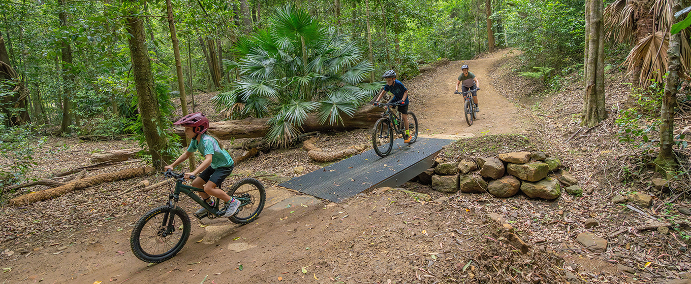 Three young kids ride across a mesh bridge on Kembla mountain bike trails. Credit: John Spencer © DCCEEW