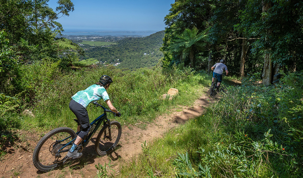 Two riders on Kembla mountain bike trails with incredible views over the escarpment down to the ocean. Credit: John Spencer © DCCEEW