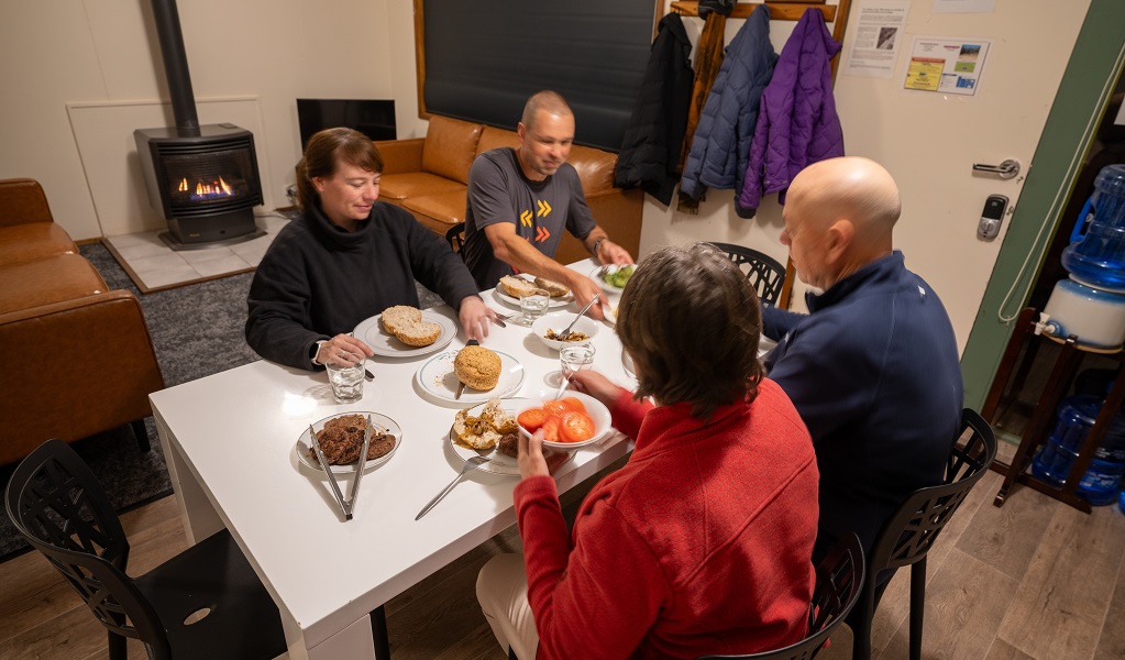 Four people enjoying dinner together in a cabin, Binda Bush Cabins, Jenolan Karst Conservation Reserve. Photo: Jenolan Caves &copy; DPE 