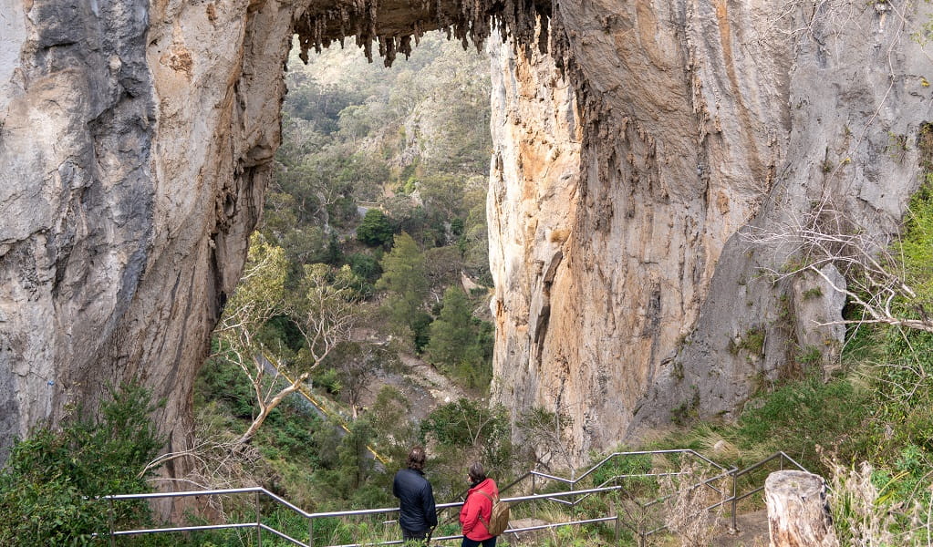 Two walkers standing under the mighty Carlotta Arch in Jenolan Karst Conservation Reserve. Photo: Jenolan Caves &copy; DPE