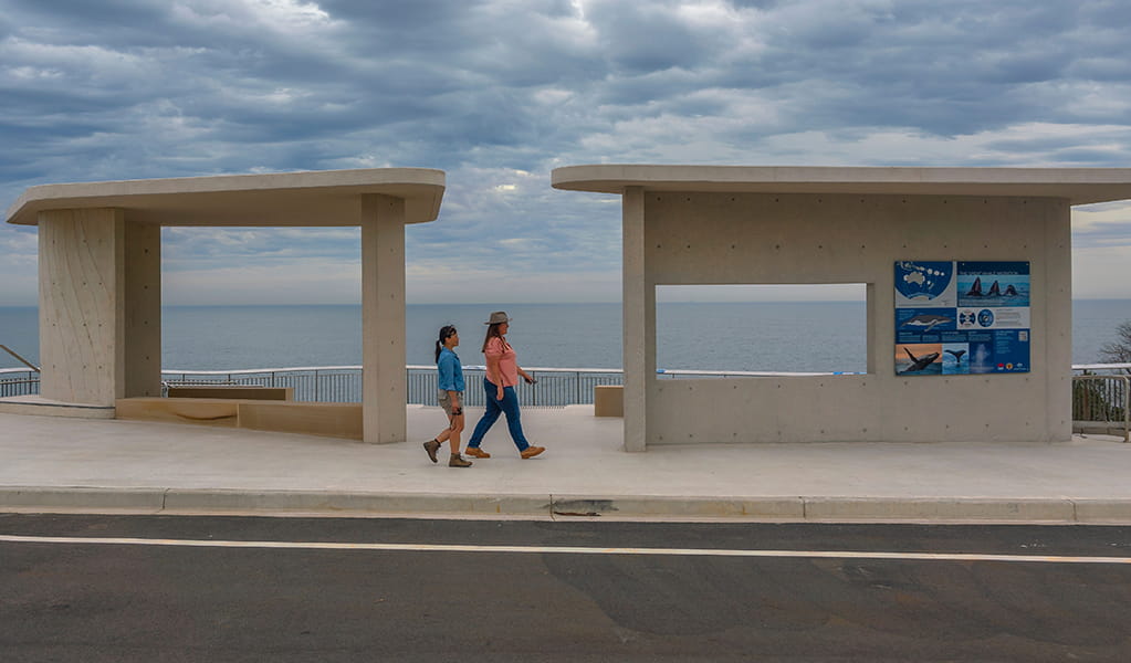 Two women walking towards whale information posters at Cape Solander lookout with ocean views. Photo: John Spencer &copy; DPE