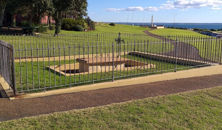 Fenced area with tomb and metal cross, on a wide grassy slope with Botany Bay in the background, near Sydney. Photo: Stacy Wilson/DPIE