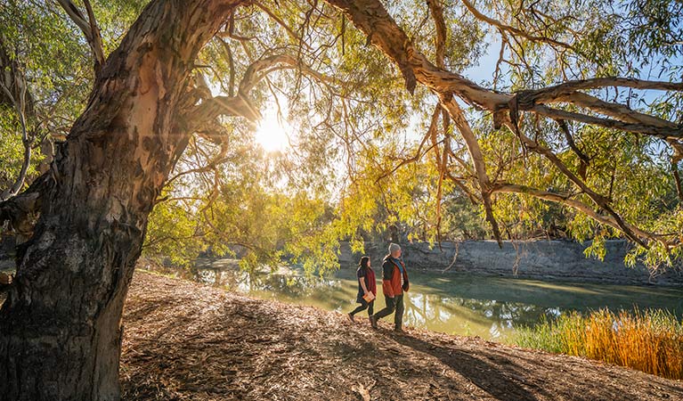 Couple walking along the river bank at sunrise, Darling River campground. Photo: John Spencer/DPIE