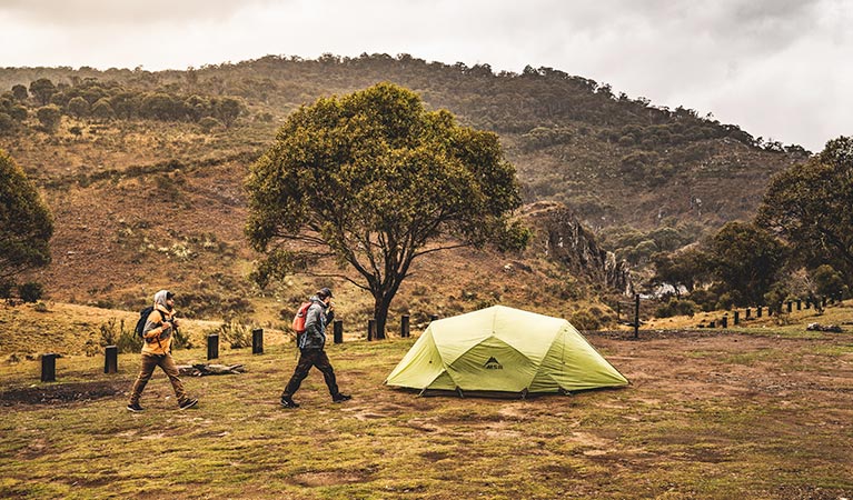 Two men walk past a green tent at Blue Waterholes campground, Kosciuszko National Park. Photo: Robert Mulally/DPIE