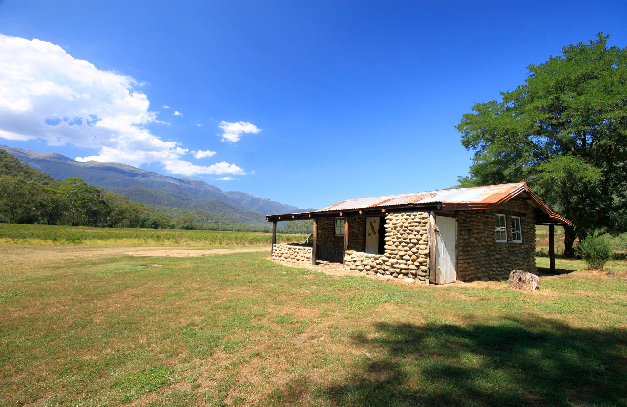 Historic hut on a grassy plain with mountains in the background. Photo: Elinor Sheargold/OEH.