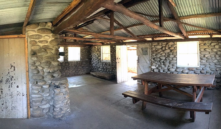 Interior of historic Keebles Hut showing stone walls, roof beams, and picnic table, Kosciuszko National Park. Photo: Elinor Sheargold/OEH.