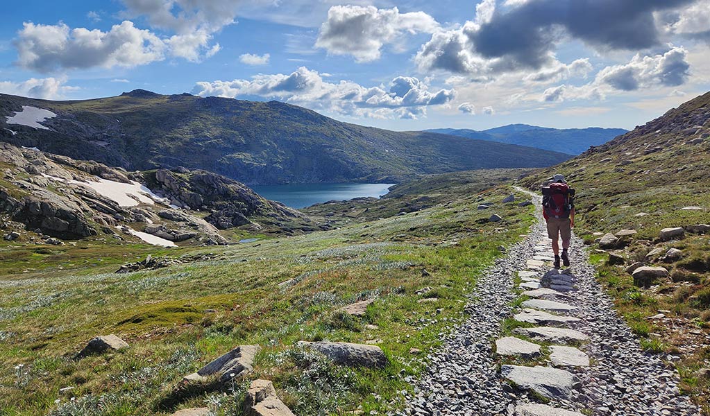 A hiker walking along Main Range Walk in Kosciuszko National Park with Blue  Lake and mountains in the background. Credit: Hayley Eriksson &copy; DCCEEW