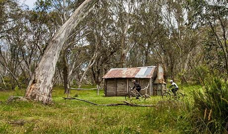Two mountain bike riders cycle past Cascade Hut, in remote Kosciuszko National Park. Photo: Murray Vanderveer/DPIE
