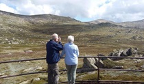 A couple take in the alpine landscape from the viewing platform of Kosciuszko lookout in Kosciuszko National Park. Photo: Luke McLachlan &copy; DPIE