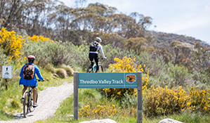 Two mountain bike riders pass a sign on Thredbo Valley track, Kosciuszko National Park. Photo: Boen Ferguson/DPIE