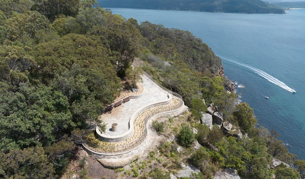 Aerial view of the curved West Head lookout, at the edge of a cliff above calm water below. Credit: Drew Elliot &copy; DCCEEW