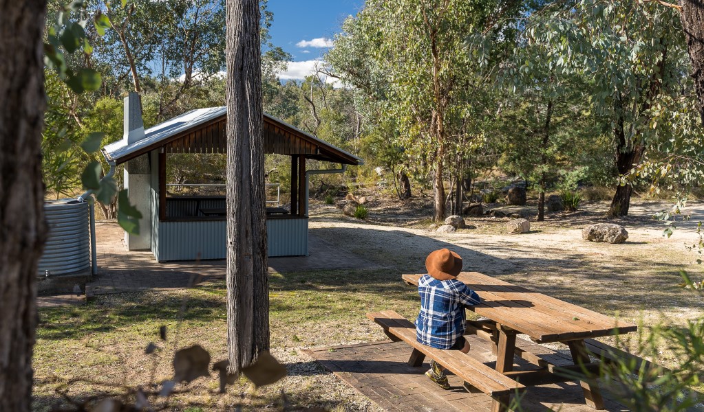 A person sitting at a picnic table next to a shelter and water tank at Macintyre Falls picnic area in Kwiambal National Park. Photo &copy; DPE