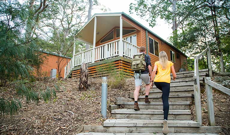 Two people walking up their stairs towards their cabin at Lane Cove cabins. Photo: Caravel Content/OEH