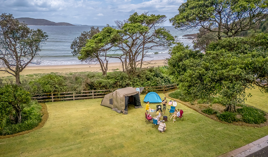 Man sitting beside his tent looking out at the ocean, at Limeburners Creek National Park. Photo: John Spencer/OEH