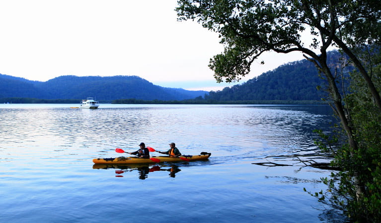 Hawkesbury River scene of 2 kayakers in a double kayak, with a river boat in the distance.  Photo: Rosie Nicolai/DPIE