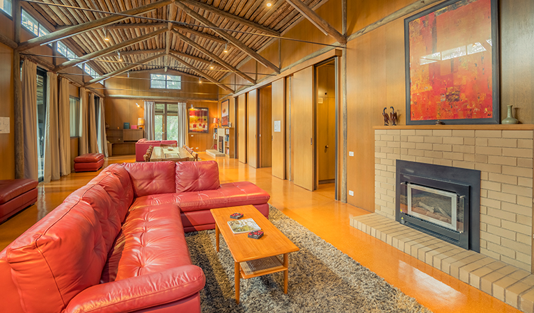 Red leather couch with a fire and rugs in the lounger room at Myer House. Photo: OEH/John Spencer