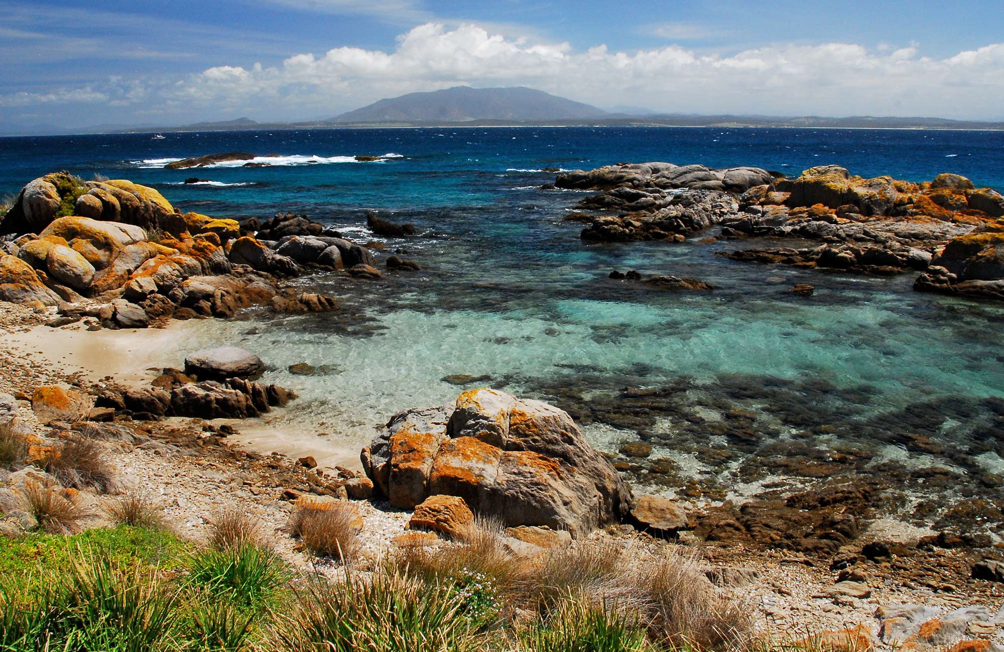Red rocks and aqua water on Montague Island foreshore with views across to Gulaga. Photo: Stuart Cohen/OEH