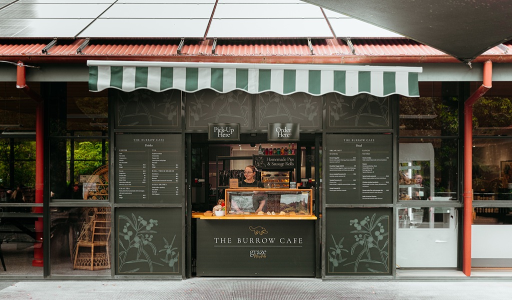 Exterior counter of The Burrow Cafe, with chalk menus and a staff member ready to take your order. The indoor area is also shown (left), Morton National Park. Credit and &copy;: Lily Crouch